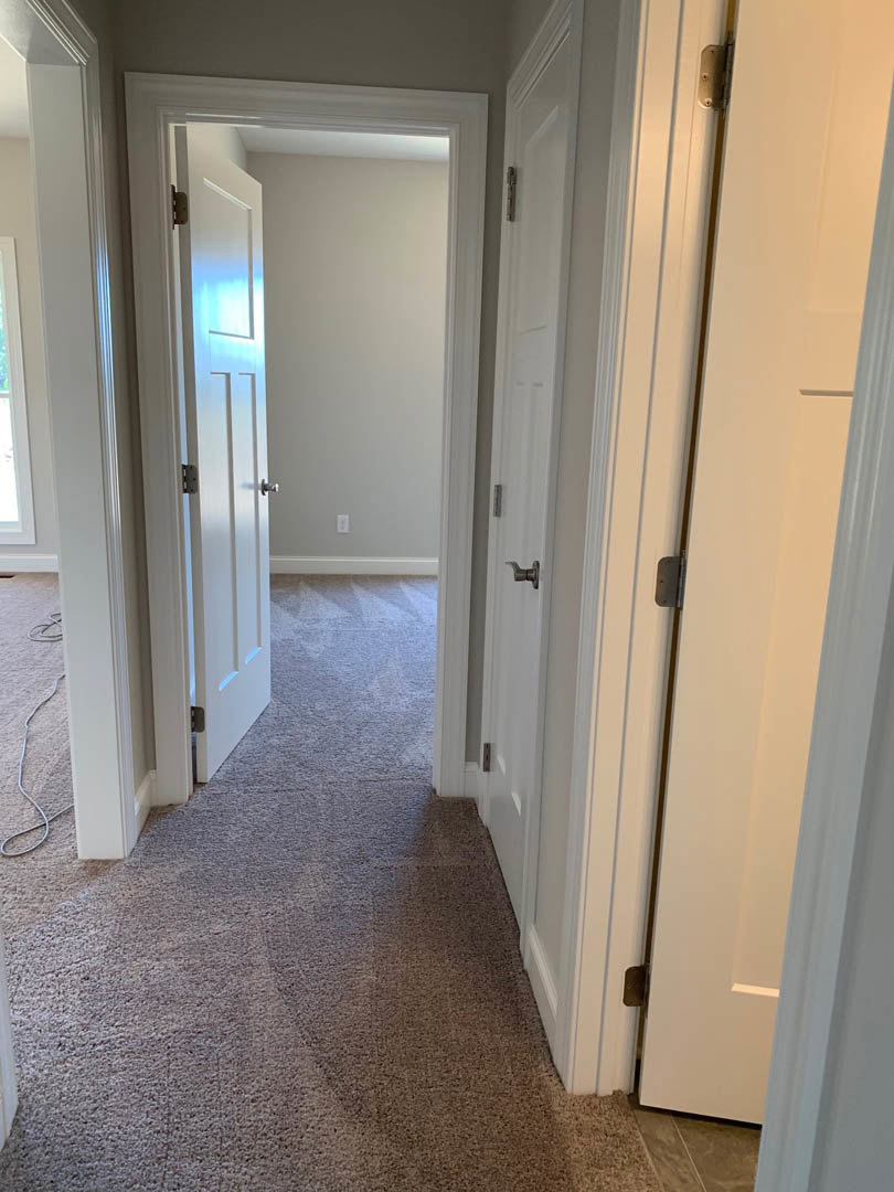 Hallway with light carpet flooring, white paneled doors, smooth white walls, and simple door hardware