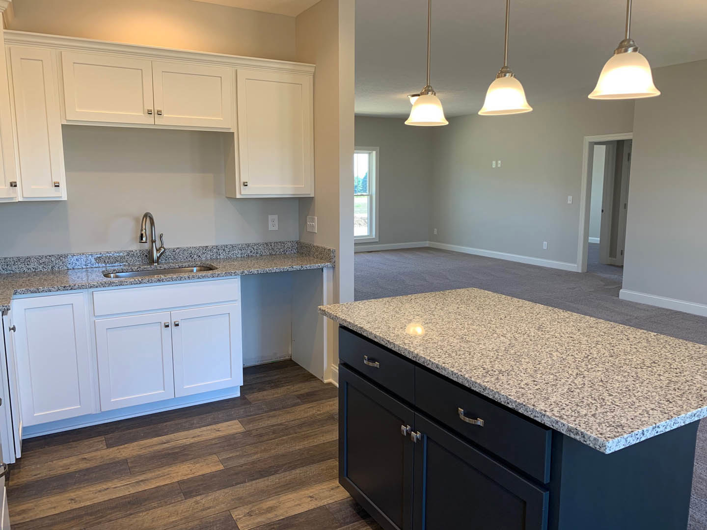 Open concept kitchen and living room featuring granite countertops, dark blue kitchen island base, white cabinets, wood flooring, white door with black hardware, illuminated