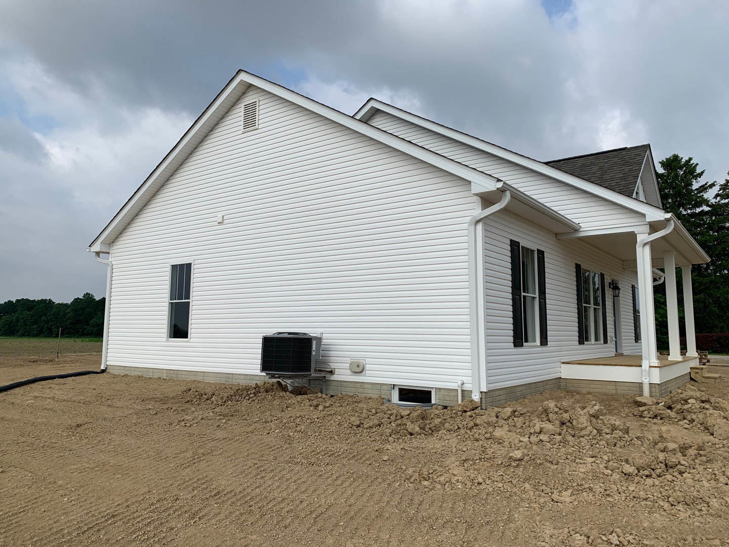 Two-story home with white siding and multiple windows, surrounded by dirt and construction materials, Rockingham Meeting House visible in the background, cloudy sky overhead.