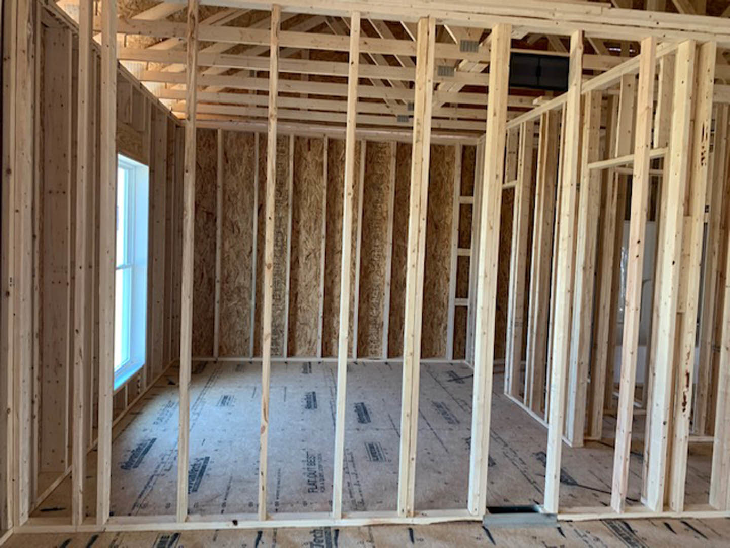 Wood-framed room under construction with two windows, exposed beams, insulation, and natural light filtering through glass panes
