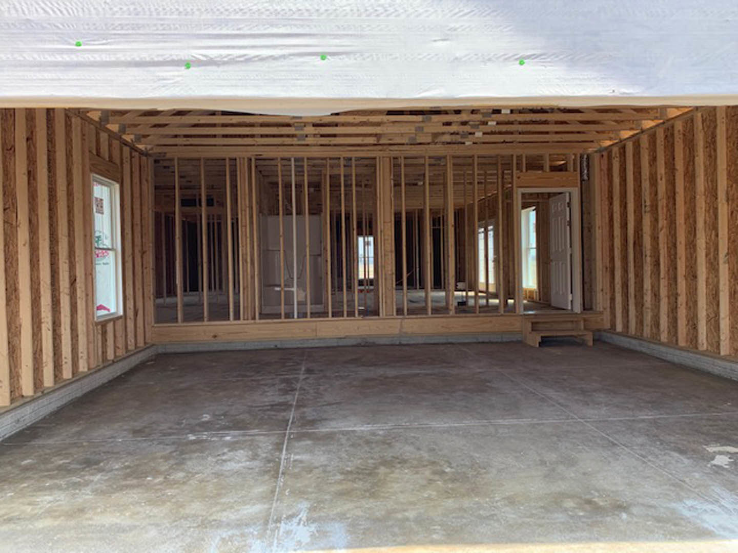 Wood-framed room under construction with exposed beams, concrete floor, white ceiling, and window letting in natural light