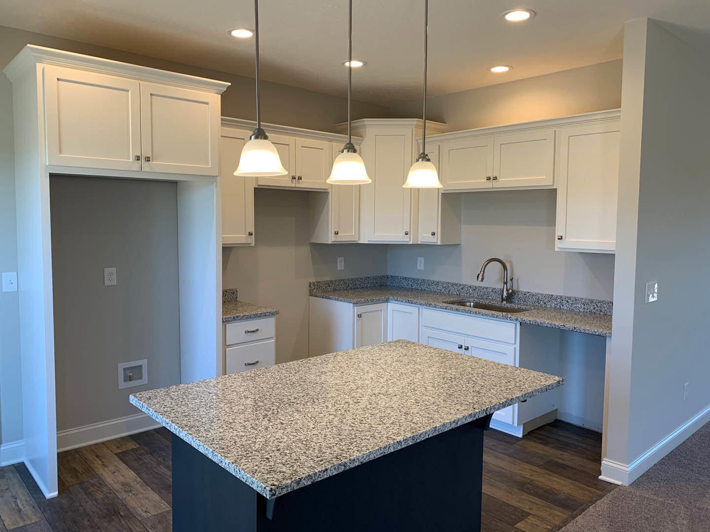Granite island with black base, stainless steel faucet, white cabinetry, tile backsplash, and white walls with a door in a modern kitchen.