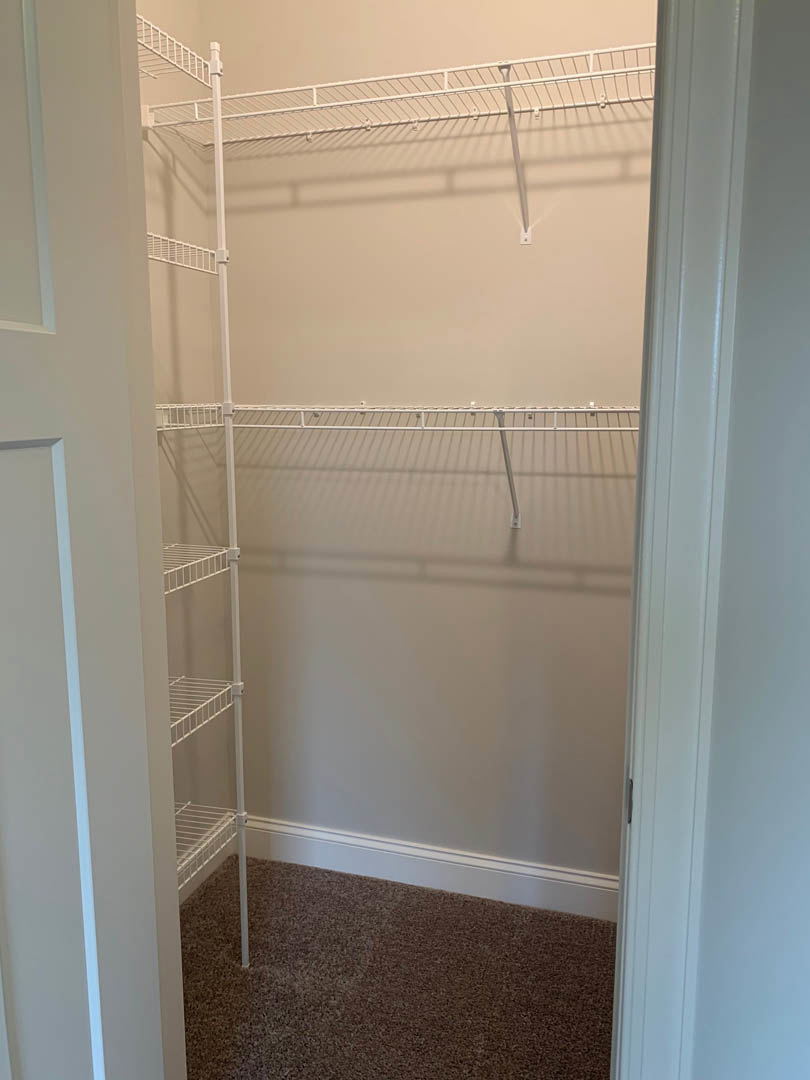 Walk-in closet with white wire shelving, white walls, and light beige carpet flooring