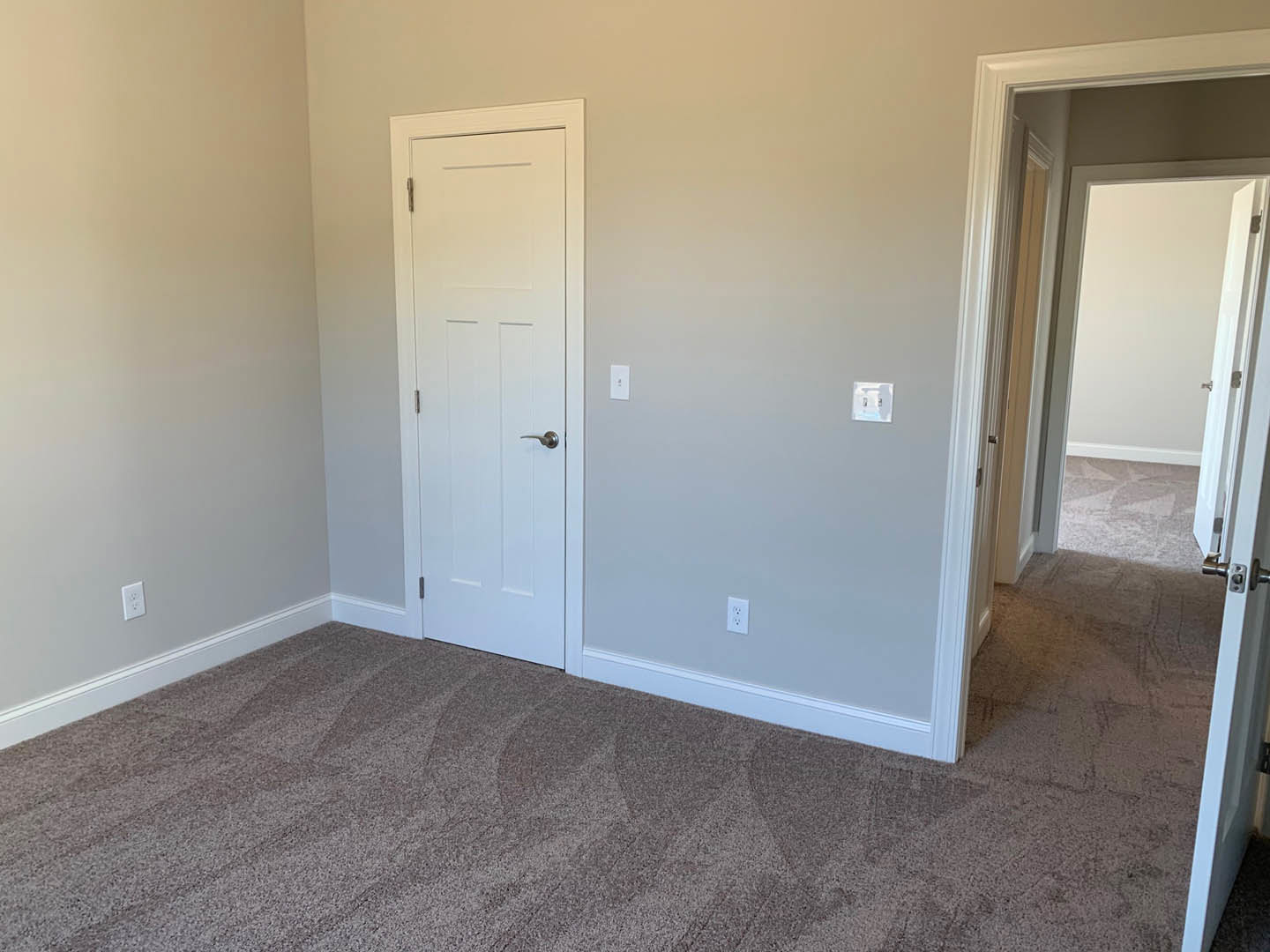 White carpeted room with white walls, white door featuring a silver handle, and a white light switch on the wall.