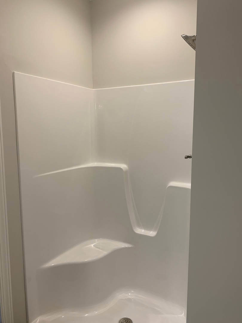 White tile shower with glass door beside freestanding bathtub, modern sink, and toilet in bright bathroom.