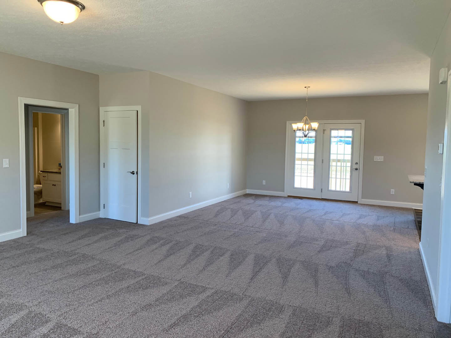 Carpeted room featuring a white door with a silver handle, double glass-paneled doors, visible doorway, and partial view of bathroom with toilet and sink