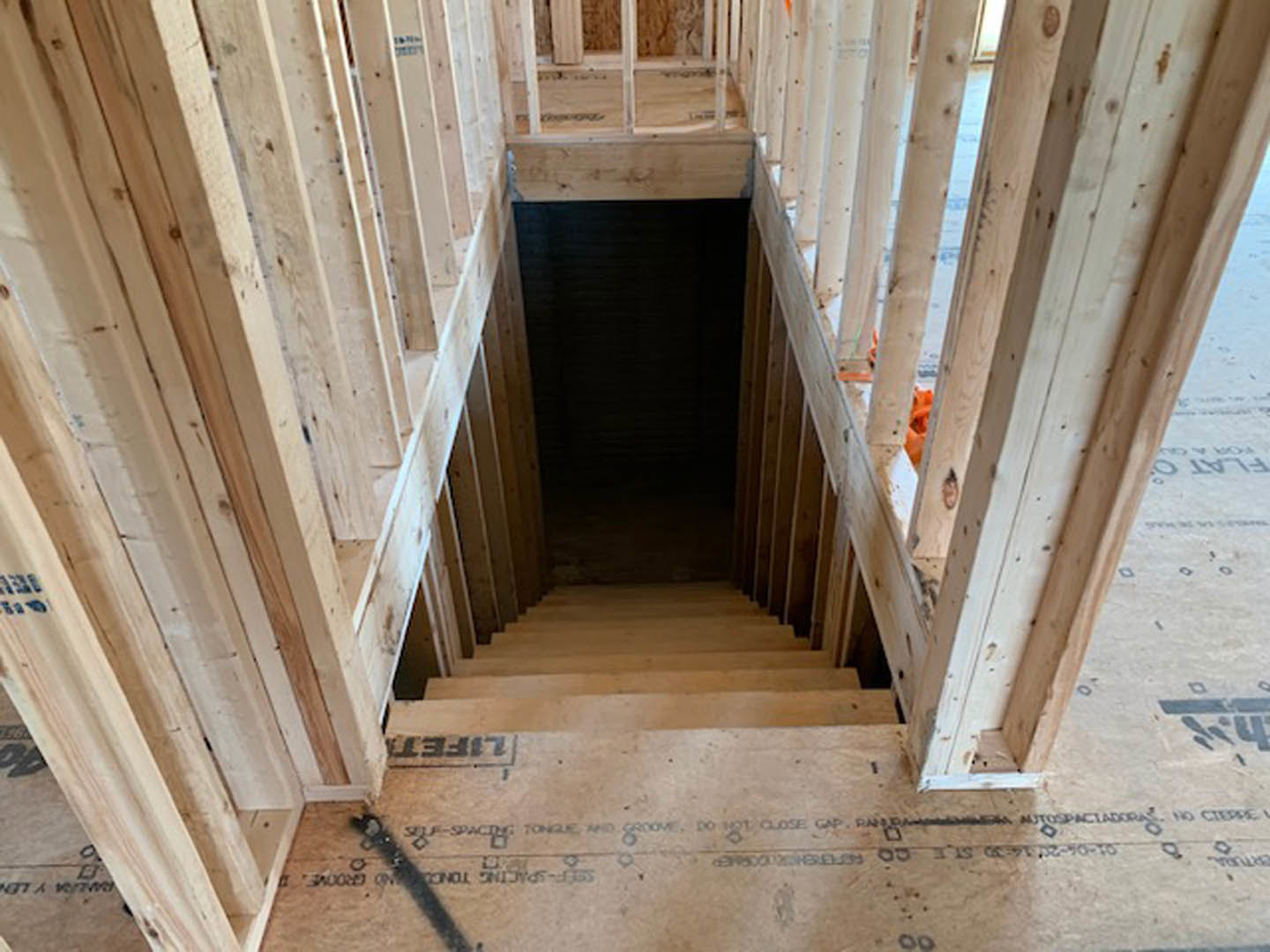 Unfinished wooden staircase with exposed beams and planks in a dimly lit room, construction materials visible throughout space