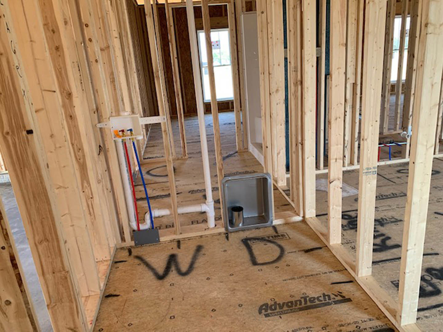 Unfinished room with exposed wood framing, plywood walls, and a window; construction materials and insulation visible.