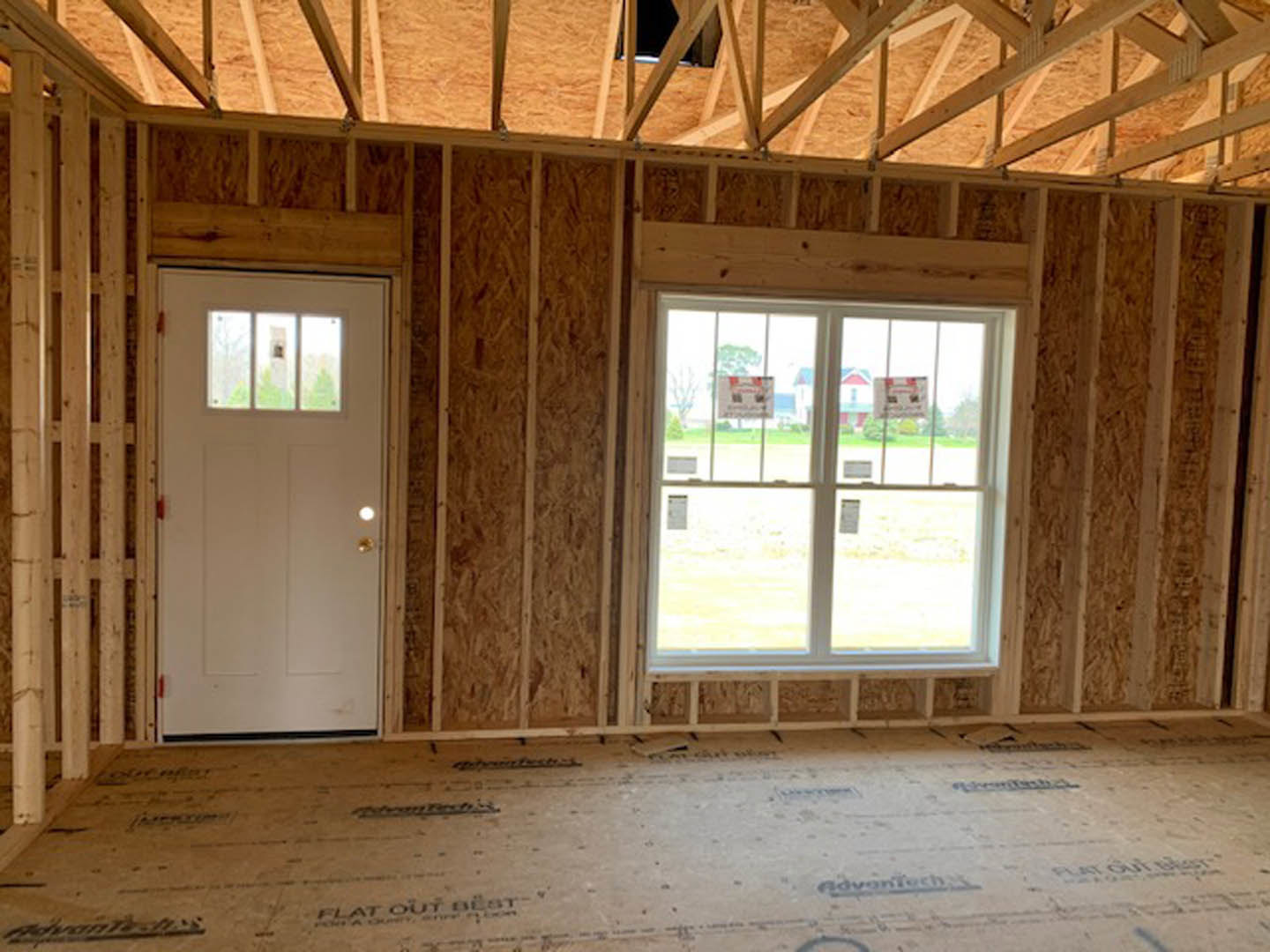 White door with glass window, large window with signage, wood plank flooring, exposed wooden ceiling beams, white walls