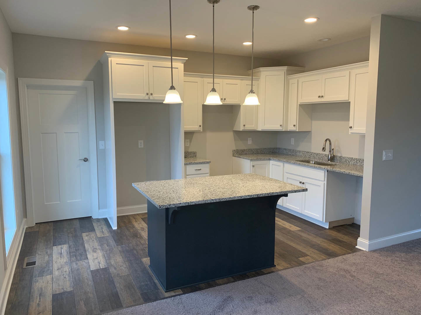 Kitchen featuring a black and white island with white cabinetry, silver handles, tile flooring, and a white door with a silver handle; modern sink and plumbing fixtures visible.