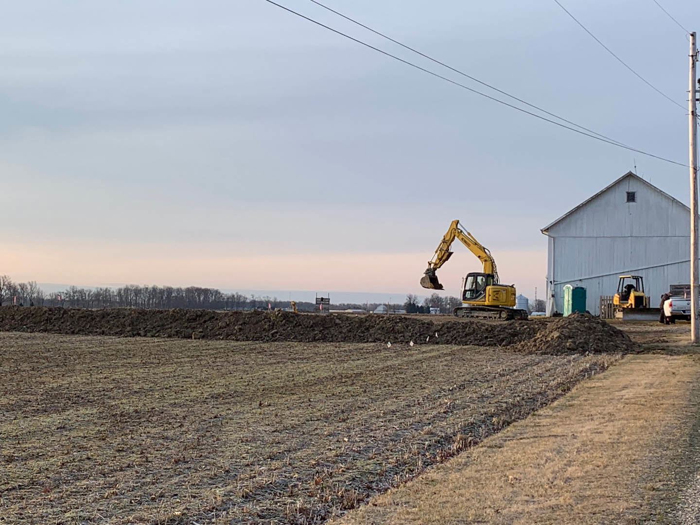 Yellow construction vehicle with bucket parked on dirt field in front of white building, under blue sky.
