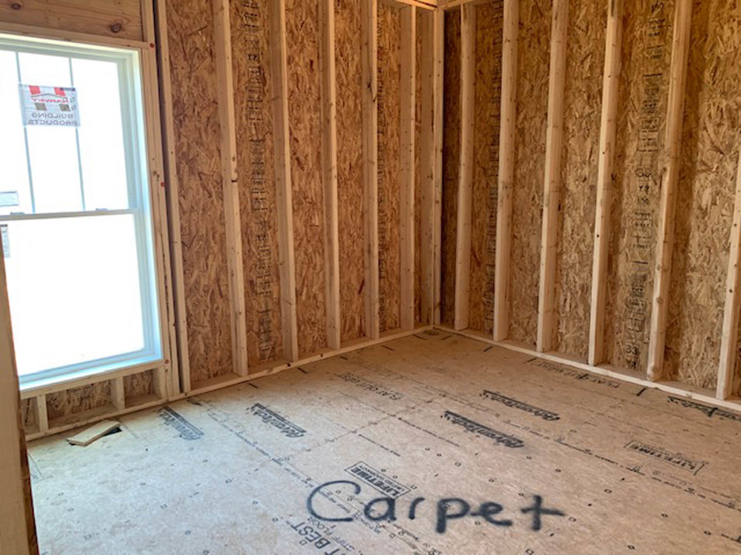 Wood-paneled room with a large window, natural plank flooring, and a white rectangular object on a table near handwritten notes and a sign.