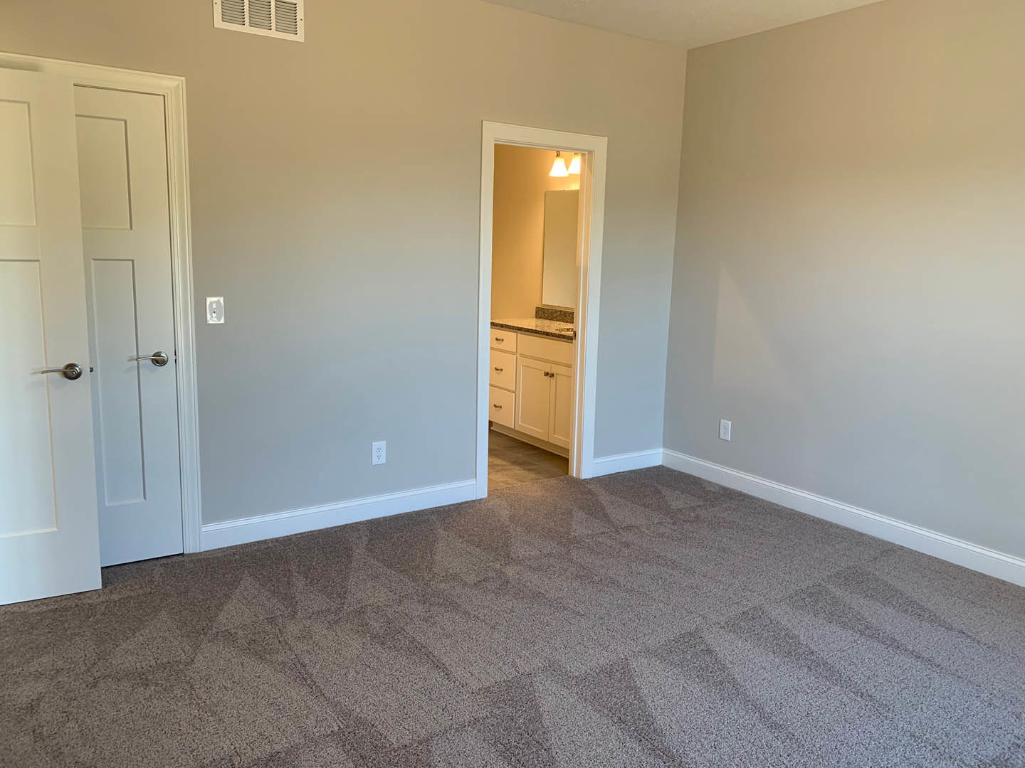 Carpeted bedroom with open white door, brown baseboard trim, and adjacent bathroom featuring marble countertop