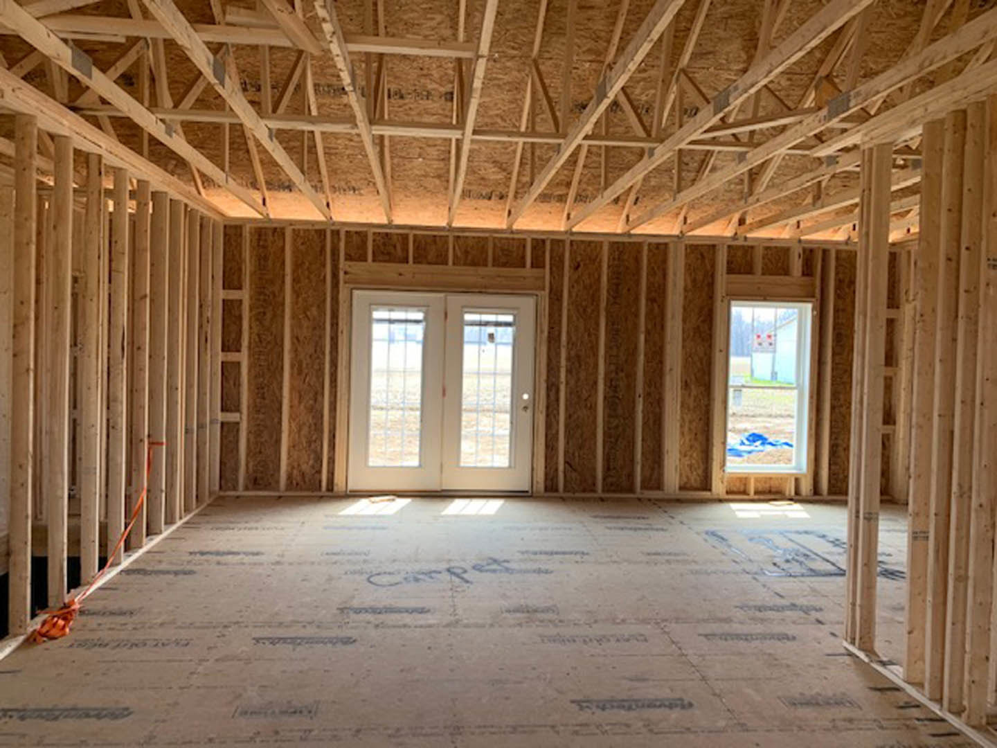 Double glass doors and large windows in a carpeted room, exposed wooden ceiling beams, natural light highlighting wood finishes and architectural details.