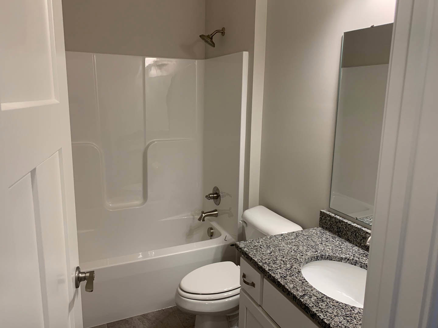 Marble countertop with oval sink and chrome faucet, white toilet with closed lid, tiled walls, frameless mirror above sink