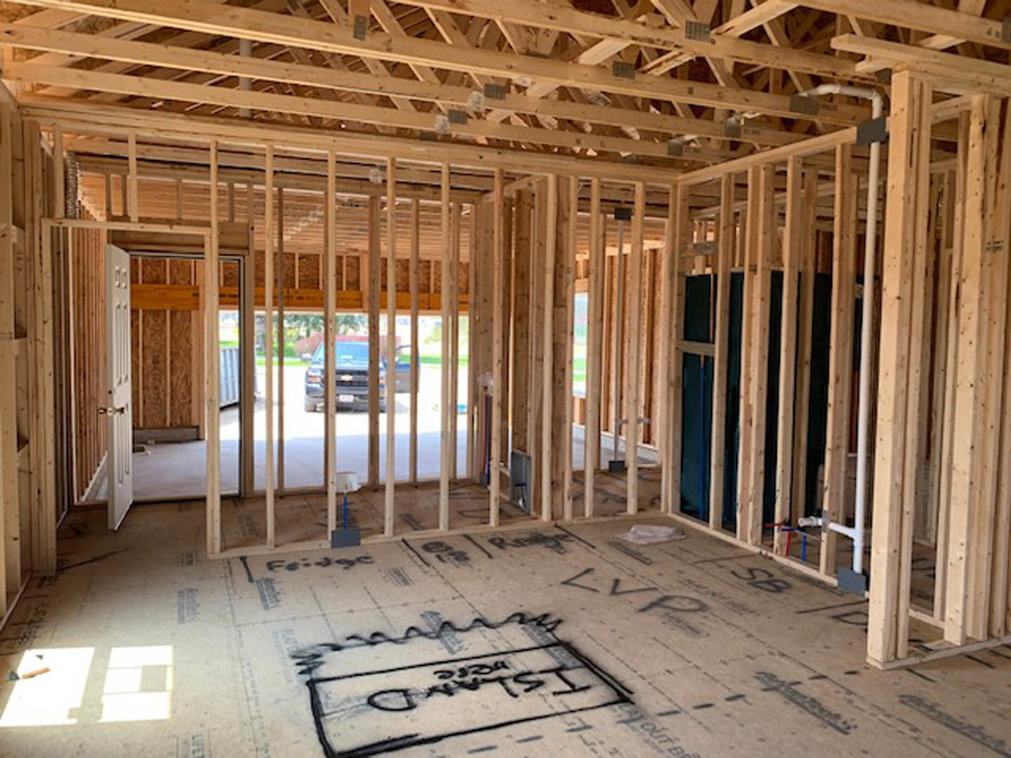 Living room with exposed wood ceiling beams, light hardwood flooring, white walls, and a wooden door