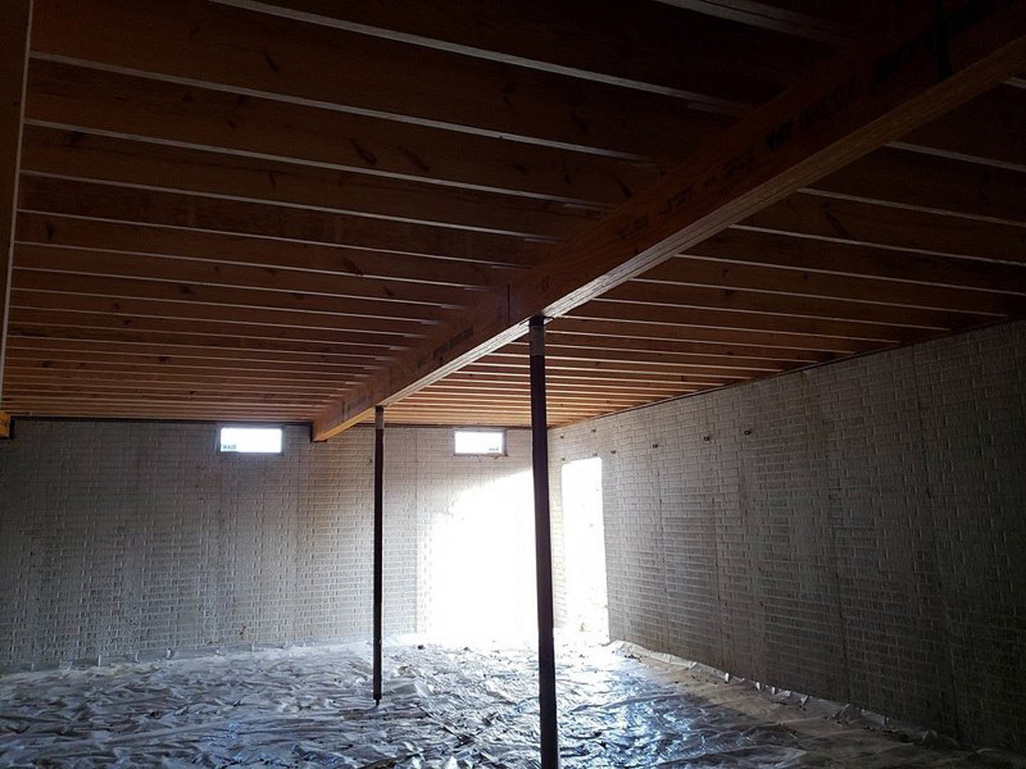 Living room with exposed wooden ceiling beams, textured brick accent wall, and natural light streaming through a window.
