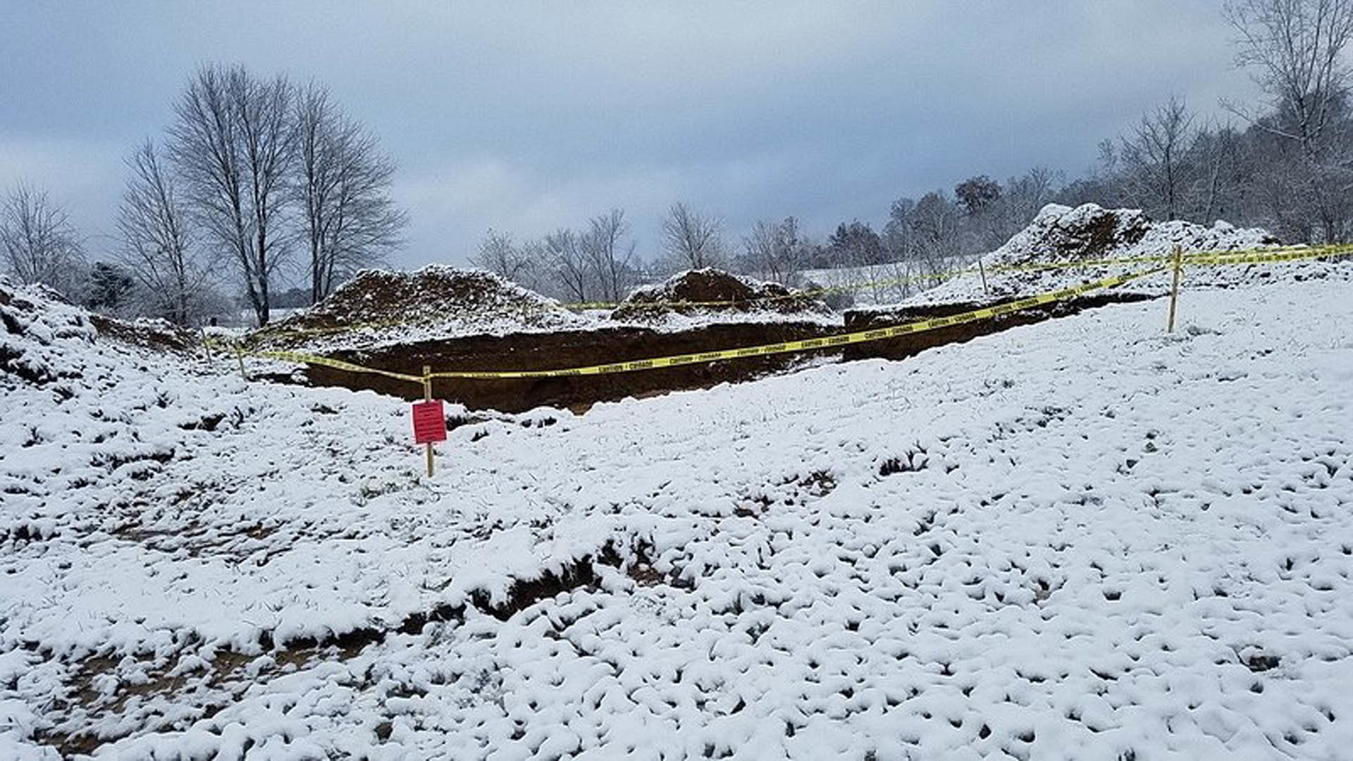 Snow-covered dirt hill with bare trees, cloudy winter sky, and frosted landscape