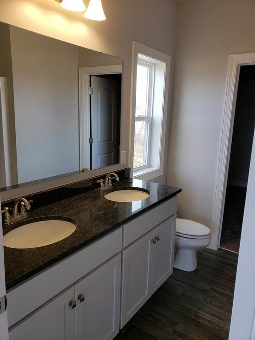 Double vanity with rectangular mirrors, undermount sinks set in a stone countertop, chrome faucets, white tile backsplash, dark wood flooring, and a window with a white frame.
