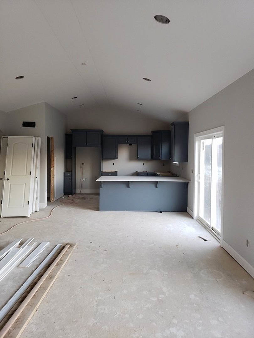 Unfinished kitchen with exposed plaster walls, white door with black frame, bare window, and partially installed countertop and shelving