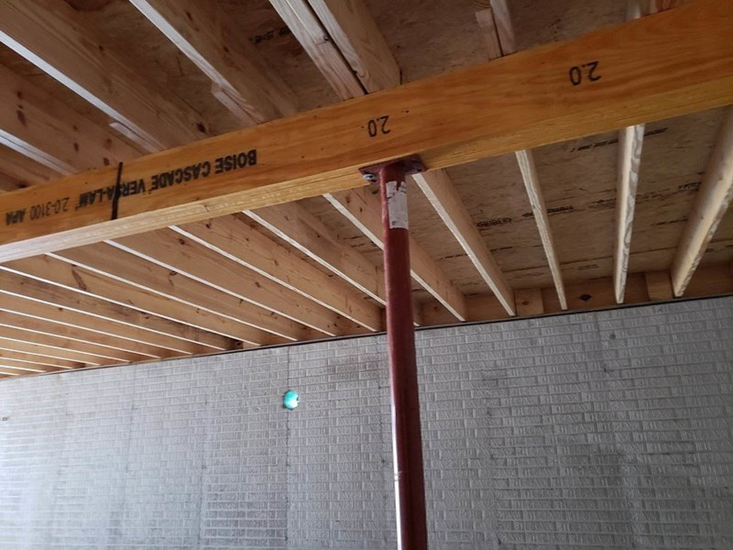 Exposed wooden ceiling beam with visible grain and black lettering, set in a room with light-colored walls and plywood finishes.