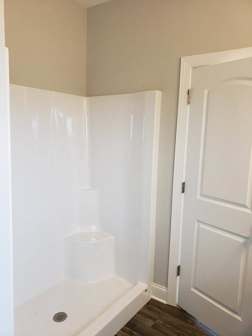 White shower stall with built-in step, wood flooring, white door, and white walls with trim in modern bathroom