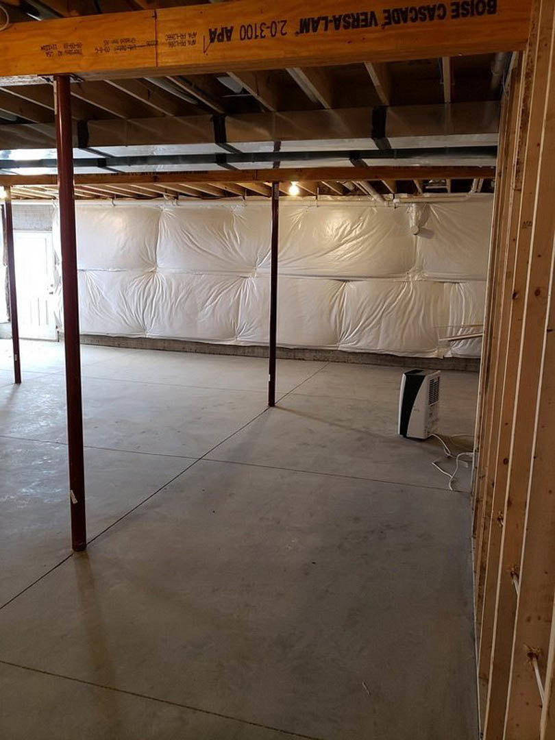 White wall with exposed wood ceiling beams, light-colored flooring, and white plastic wall covering.