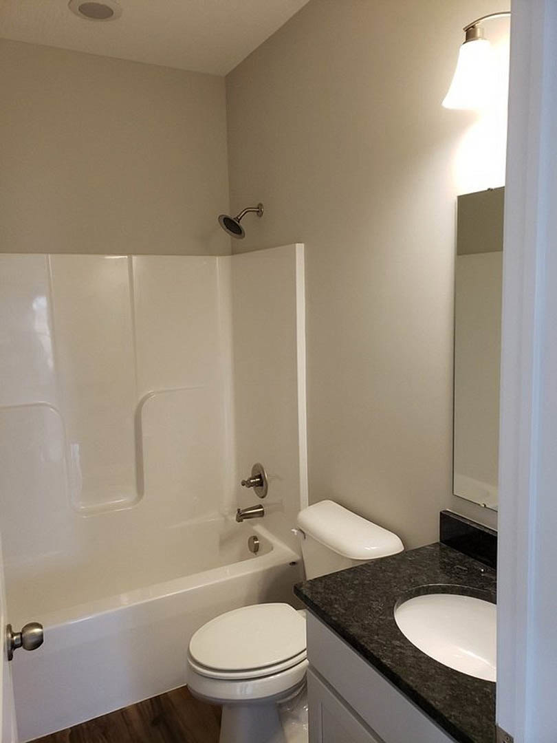 White porcelain sink, modern toilet with closed lid, and rectangular bathtub set against light gray tiled walls in a contemporary bathroom.