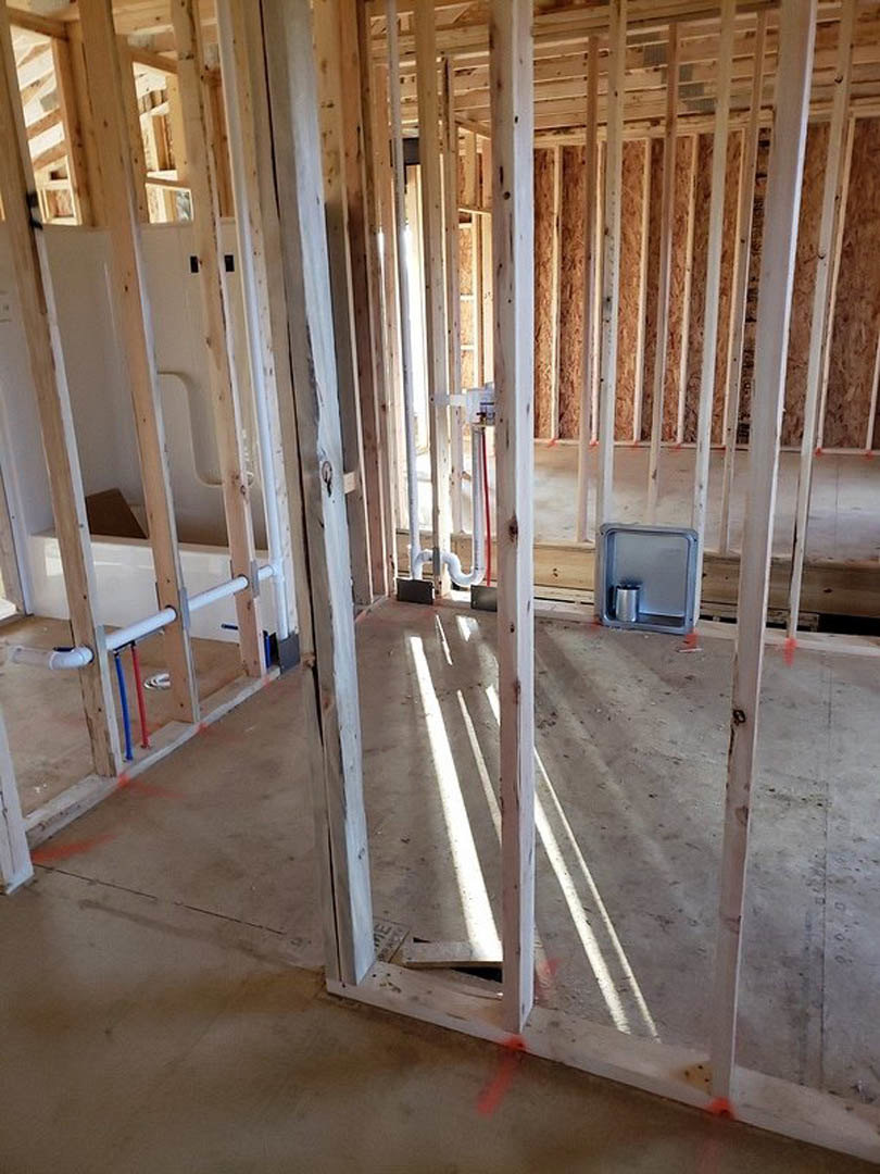 Exposed wood framing in a room under construction, red tape marking areas, metal electrical box with silver can, visible composite insulation, close-up of red, white, and blue