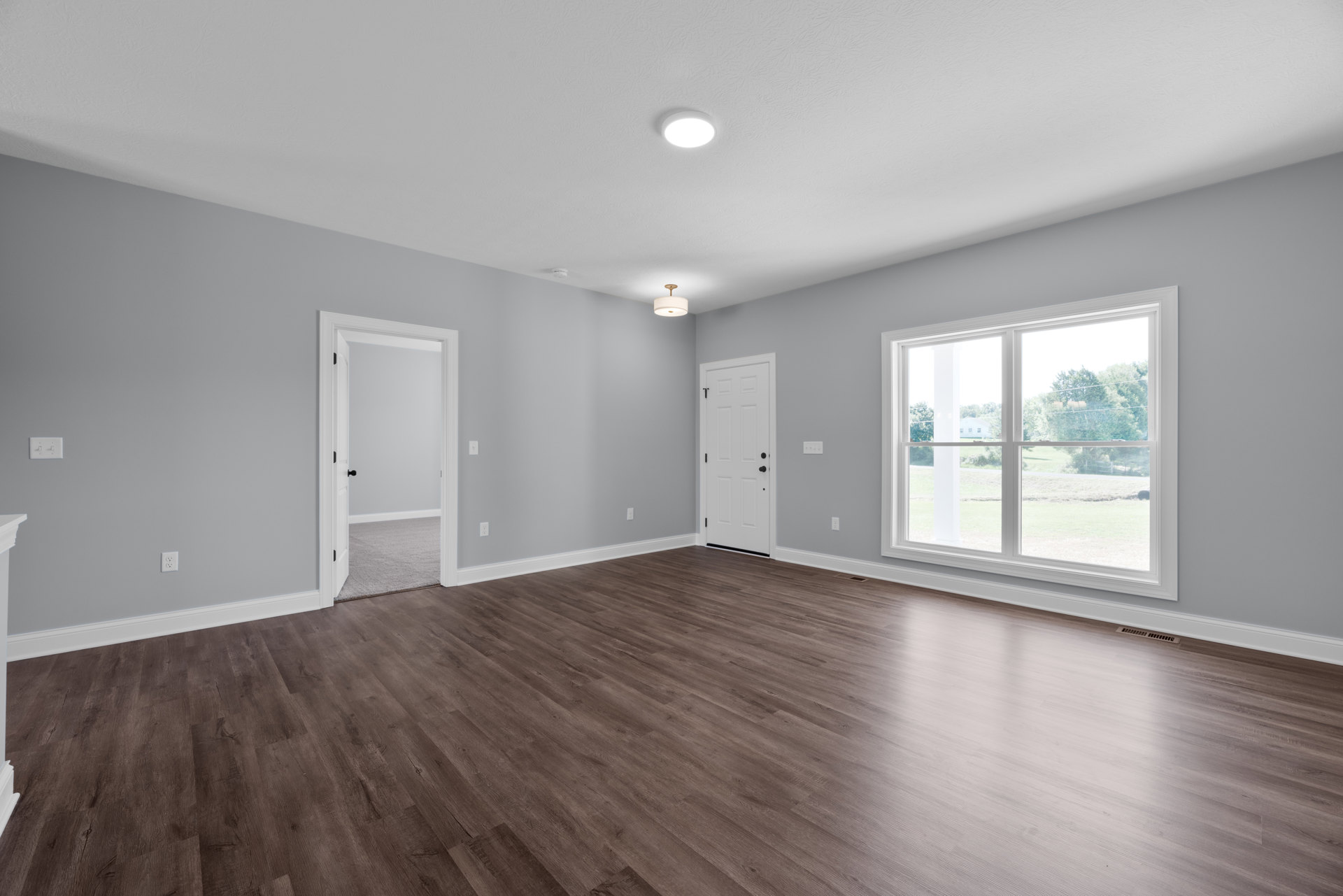 Wood floor room with white walls, large window, white door with black knob, and ceiling light fixture with white shade