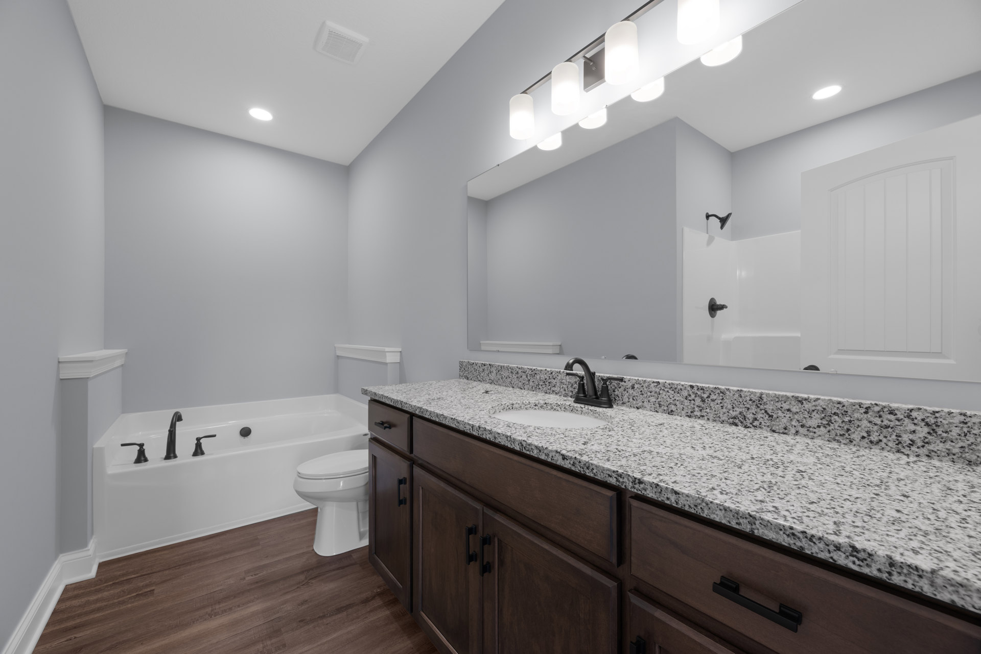 Bathroom with marble countertop, black faucet, large mirror, freestanding bathtub, white toilet, curved-top door, and modern light fixture