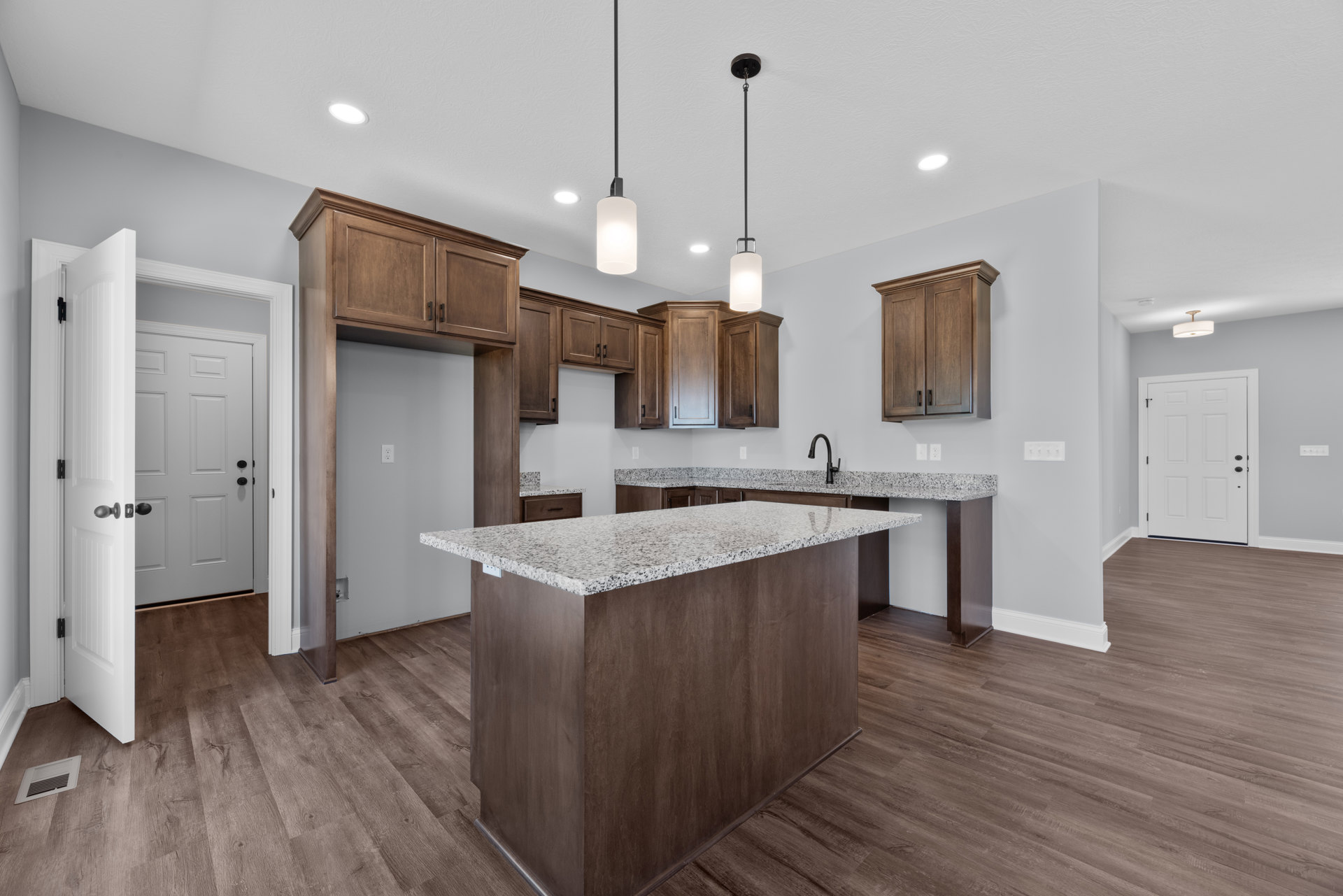 Marble kitchen countertop with wooden cabinets featuring black handles, white door, tile flooring, and a central island.