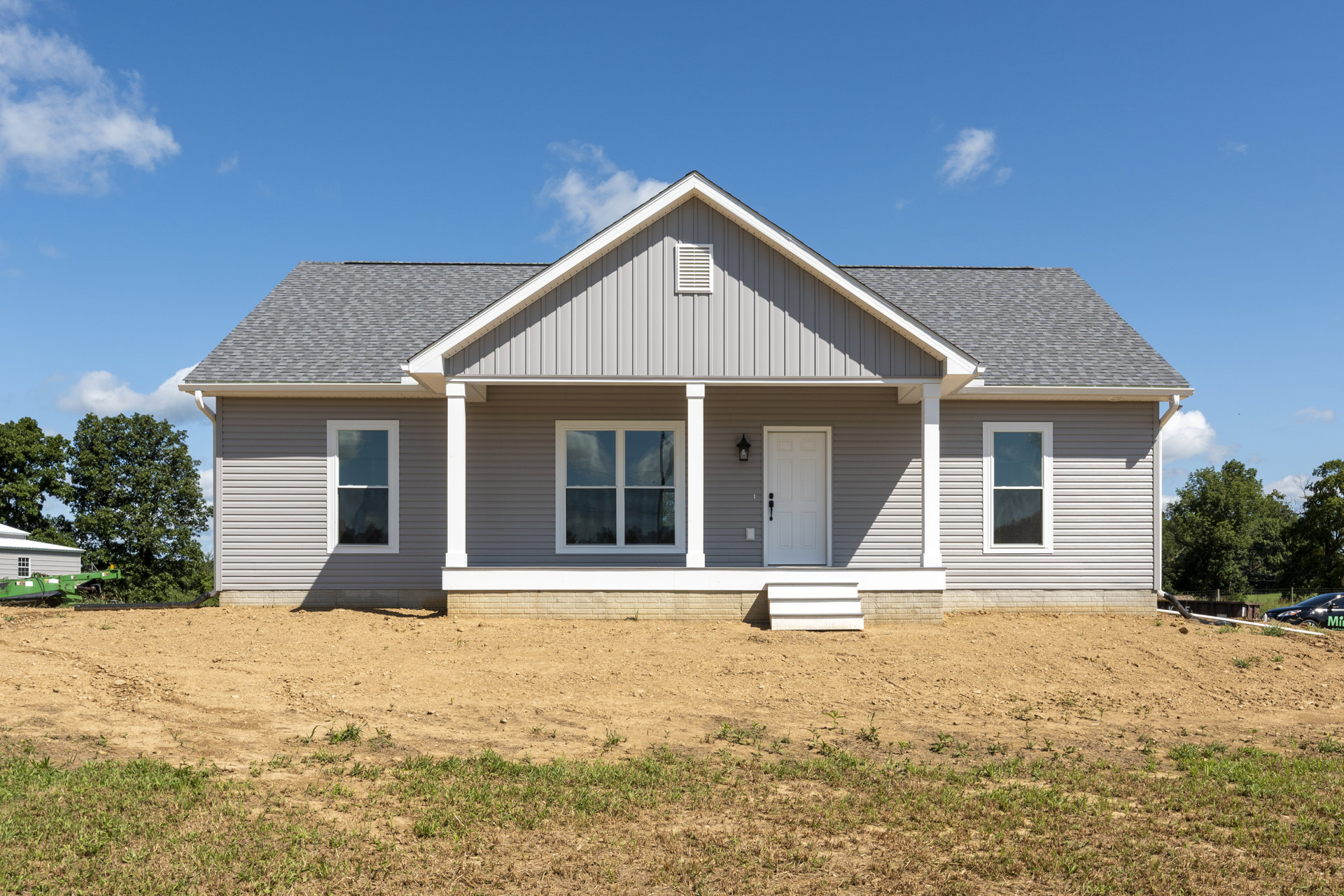 Modern house with white siding, black handle on white front door, large window reflecting clouds, white vent on exterior wall, dirt yard in foreground