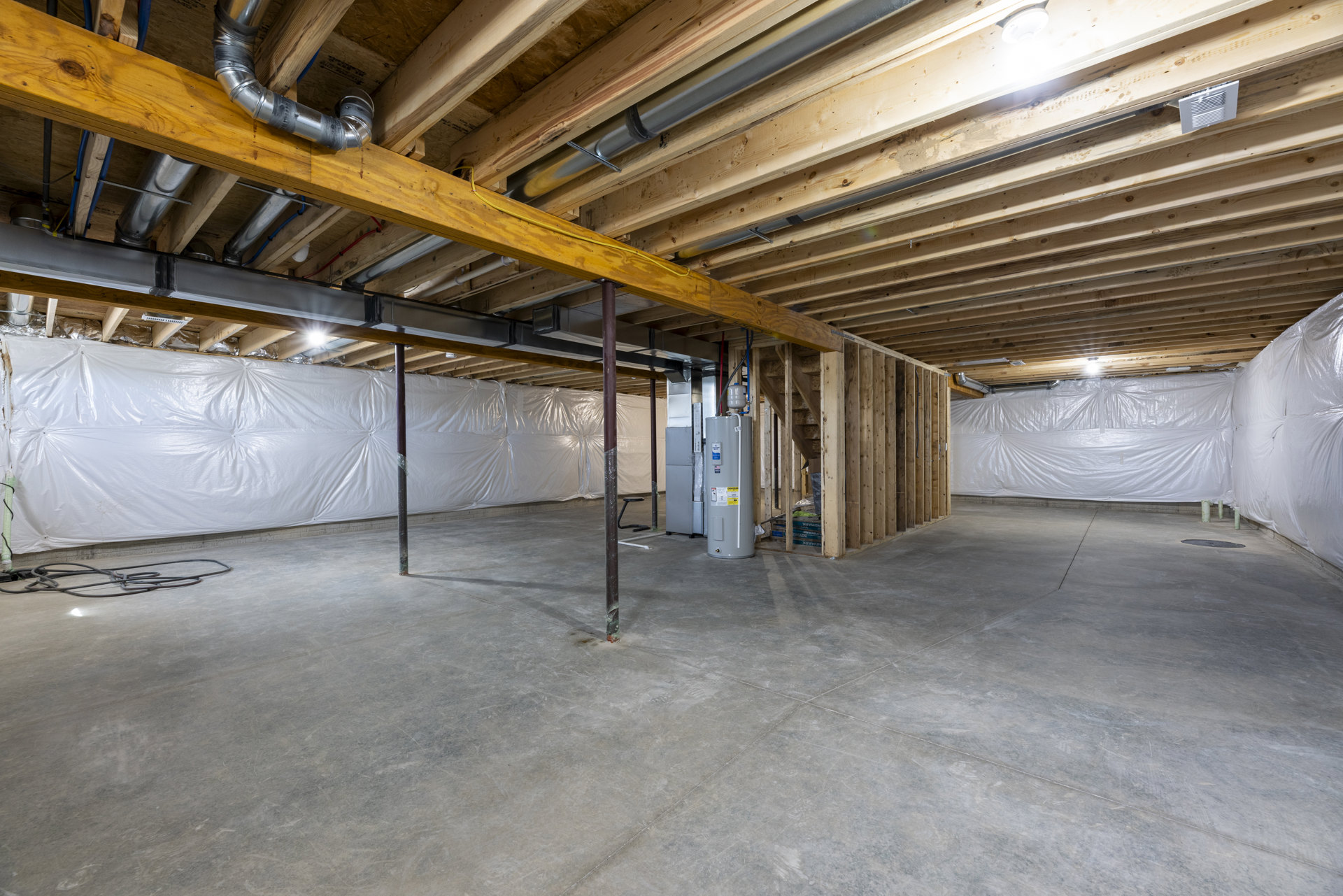 Basement room with exposed wooden ceiling, white metal support pole, concrete floor, and white vent on wood surface.