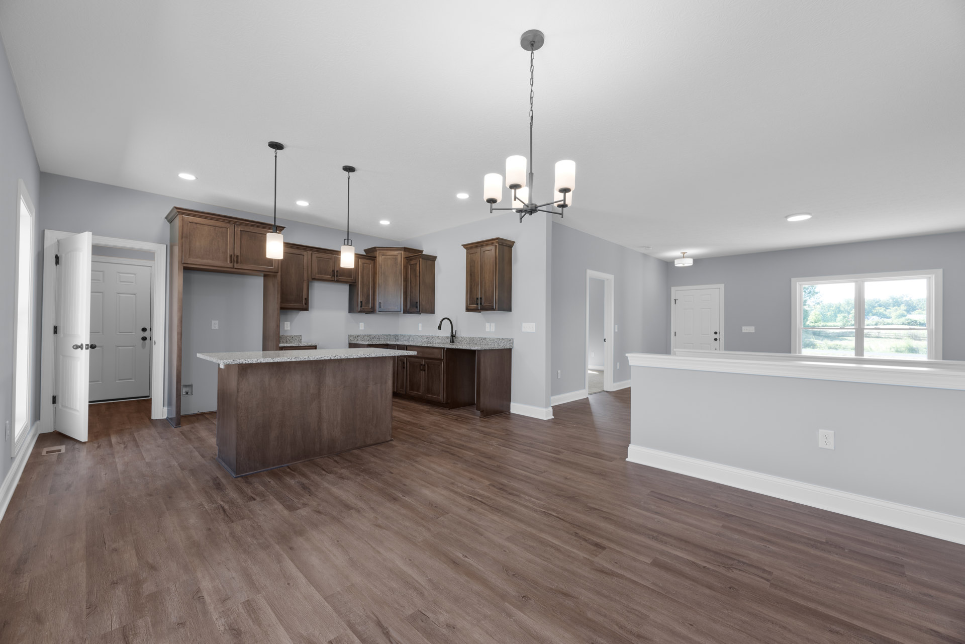 Open-concept kitchen and living room featuring hardwood floors, white cabinetry, wood island, large window with view of trees, white door with black hardware, and neutral walls.