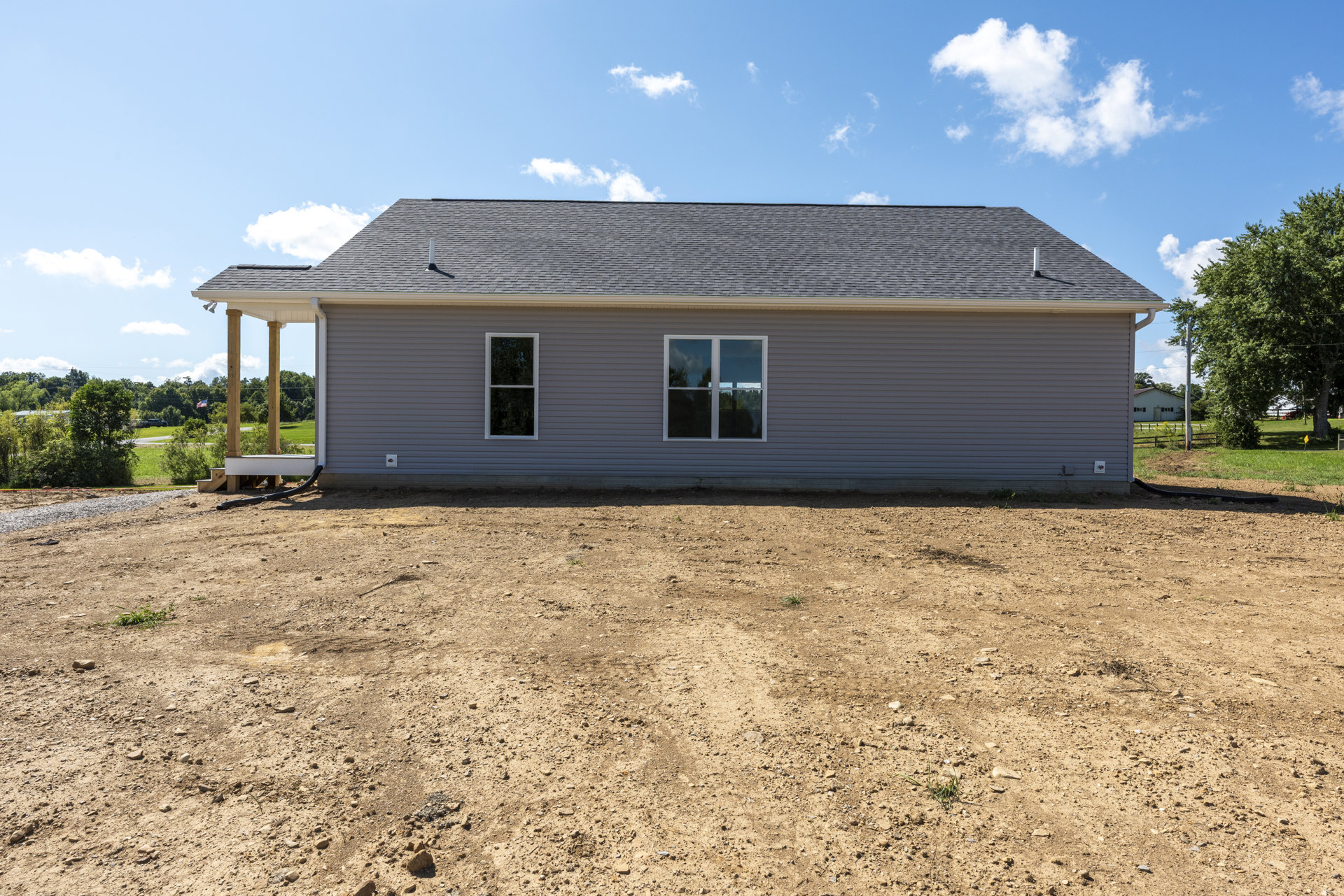 Grey custom home with white-framed windows, metal wall, and dirt yard; tree and power lines under blue sky