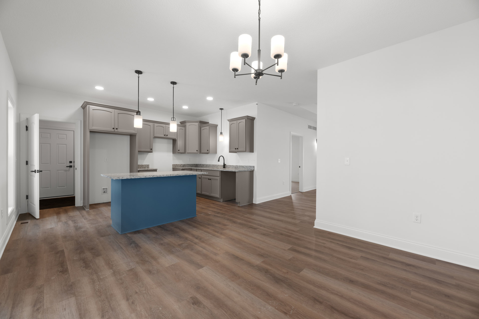 Open kitchen and dining area with wood flooring, blue island topped with marble, white cabinetry, black-handled door, white chandelier, and recessed lighting.