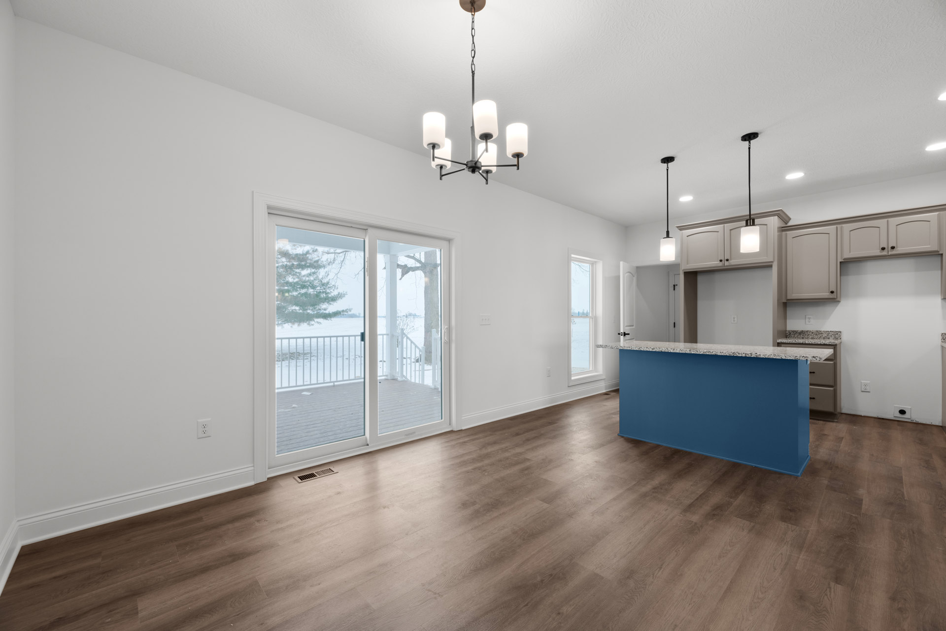 Open-concept room featuring a blue bar with marble countertop, hardwood flooring, white cabinetry, modern ceiling fixture, sliding glass doors leading to a deck overlooking a snowy