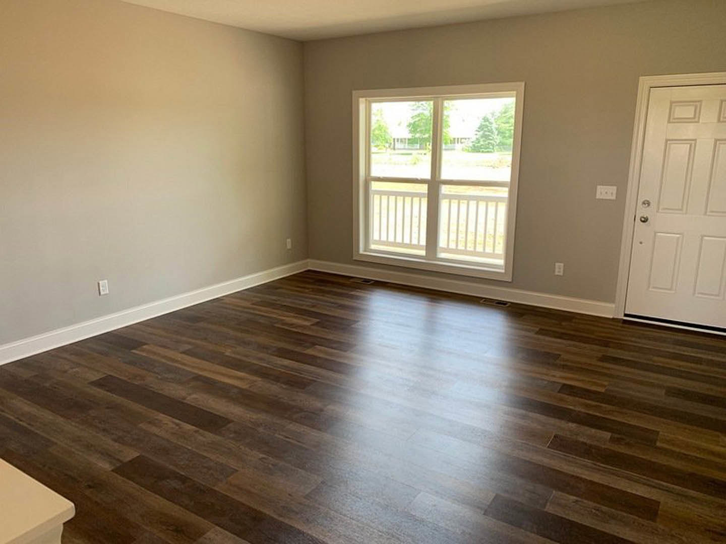 Sunlit room featuring a large window with white trim, smooth hardwood flooring, and neutral painted walls.