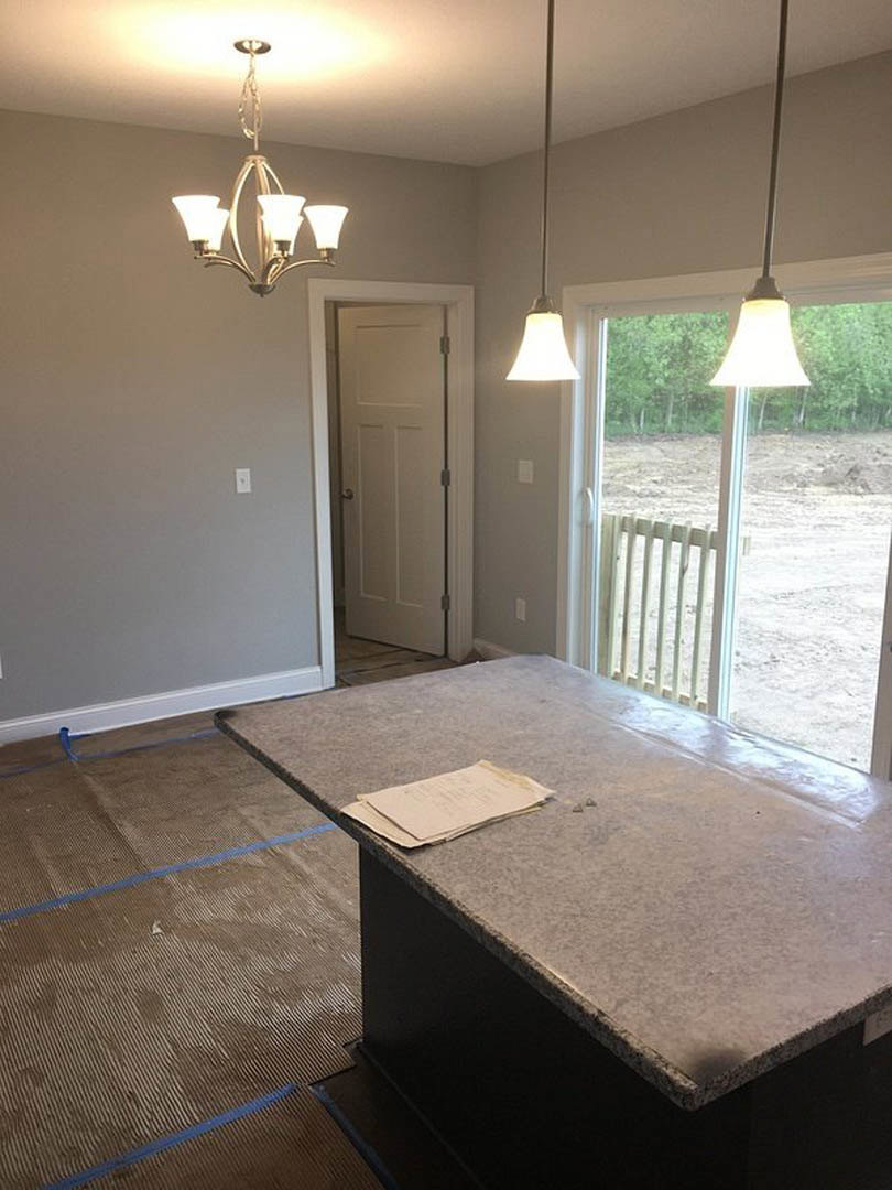 Marble table with stacked papers beneath a modern chandelier, white door with silver handle, floor lamp beside door, light wood flooring, neutral walls, and cabinetry.