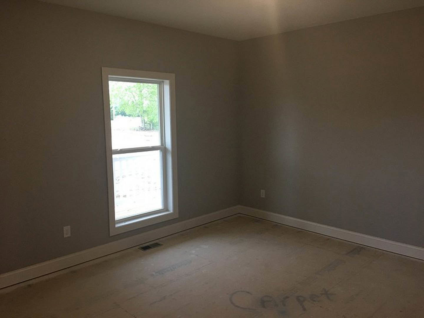 Sunlit room with white plaster walls, large window overlooking trees, and polished hardwood flooring