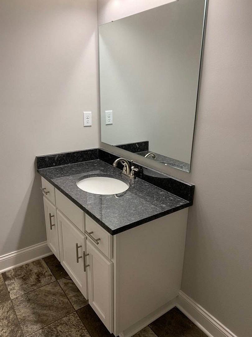 Modern bathroom featuring a large wall mirror above a stone countertop with a vessel sink, chrome faucet, tiled backsplash, and neutral tile flooring