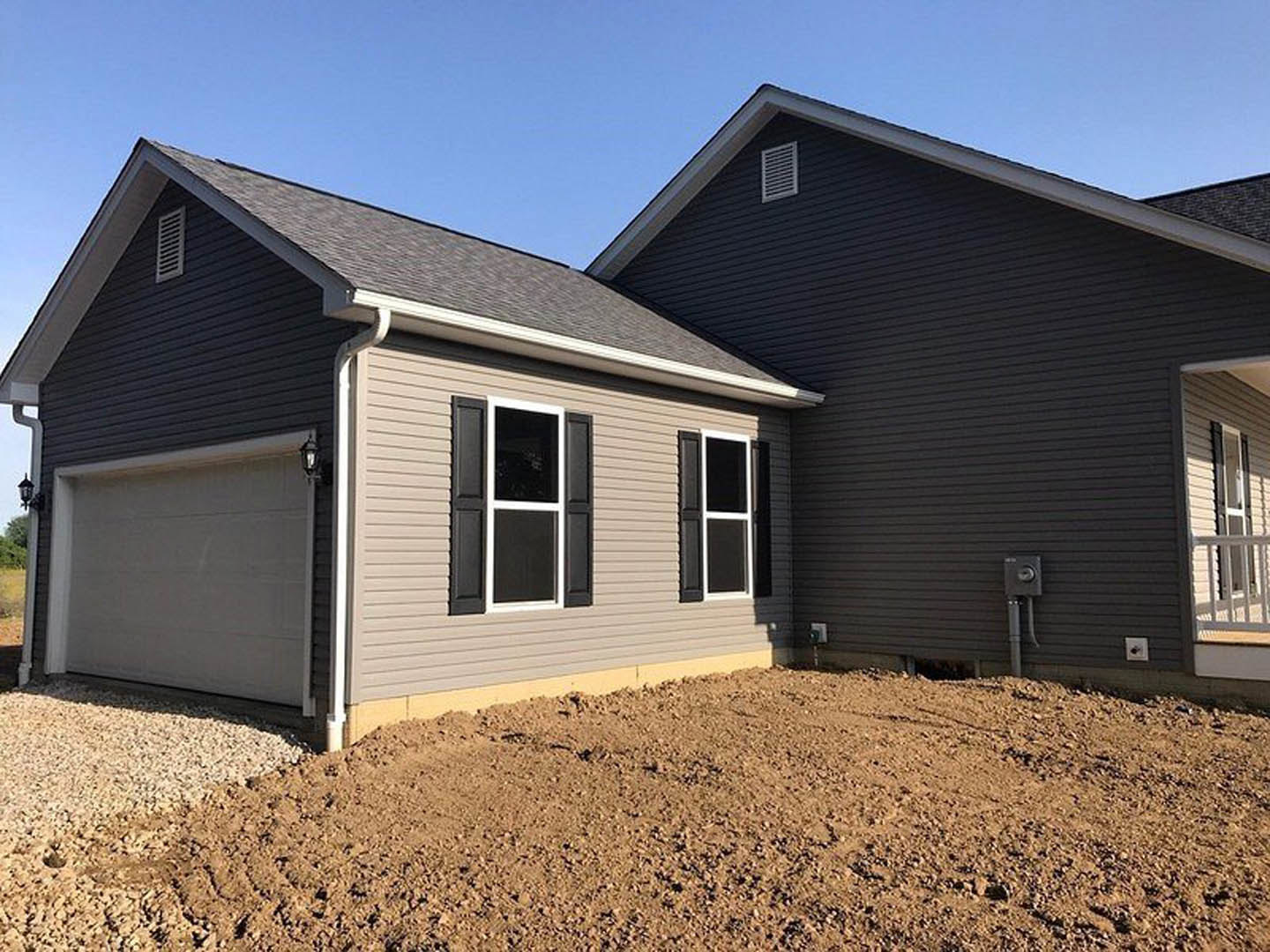 Two-story home with light siding, white-trimmed windows, attached garage featuring paneled door, exterior wall vent, dirt driveway, and lamp post near entrance