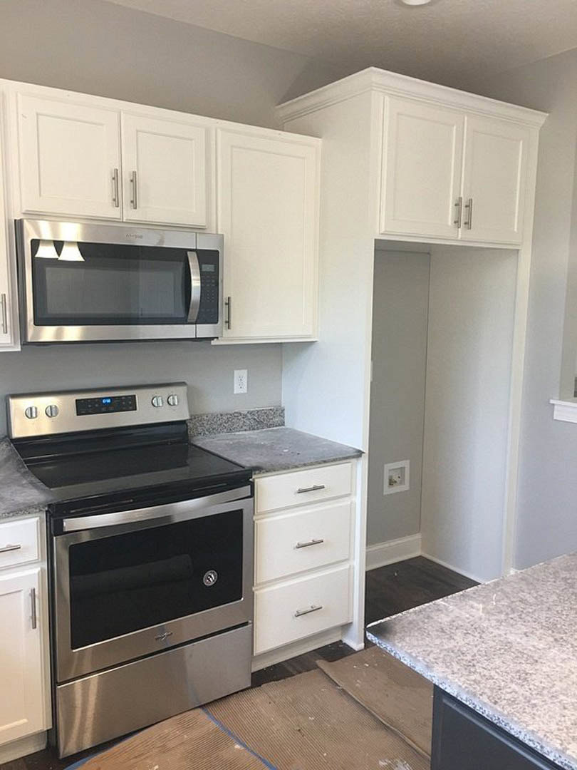 White kitchen with shaker cabinets, stainless steel oven and microwave, quartz countertop, and white tile backsplash