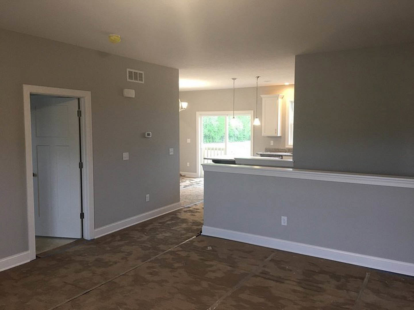 Open-concept living room with tile flooring, adjoining kitchen and dining area, white walls and trim, window with white frame, and white door with metal handle