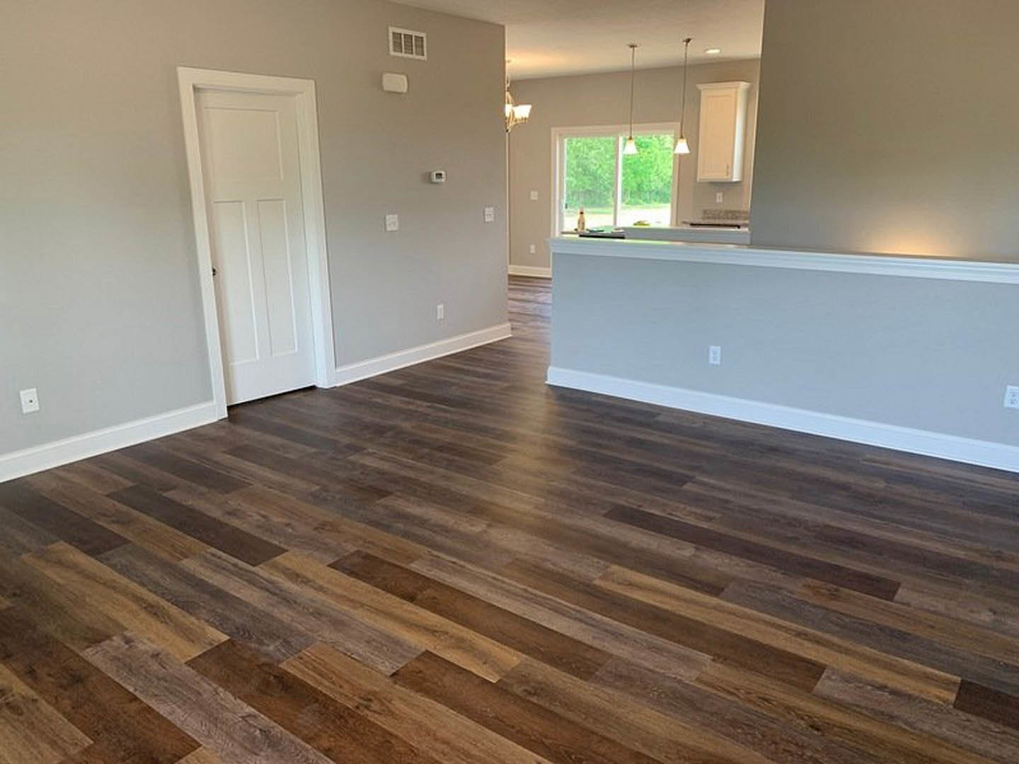 Hardwood floor room with white walls, white door featuring black hardware, grid window overlooking trees