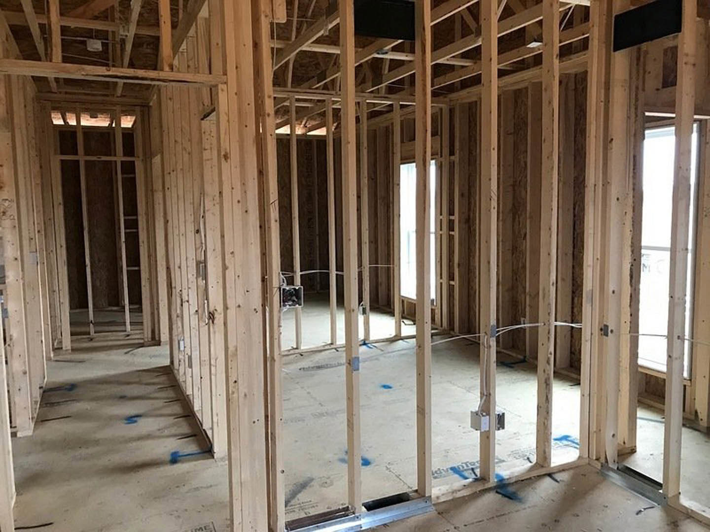 Wood-framed room under construction with exposed beams, unfinished lumber, and a window opening; shelf and black belt resting on wooden surface.