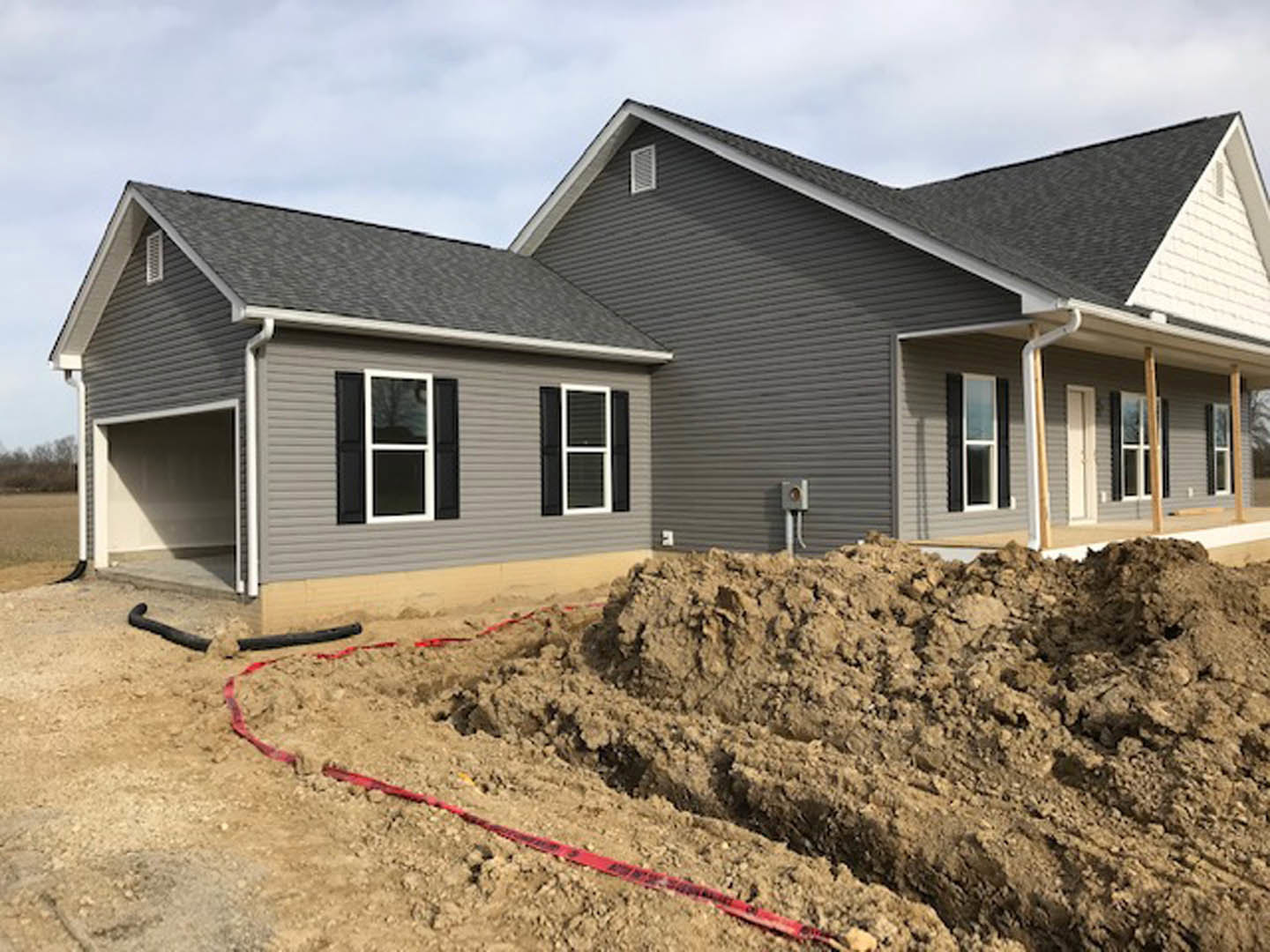 White house exterior with white-framed window and door, pile of dirt on ground, red and black hose lying near foundation