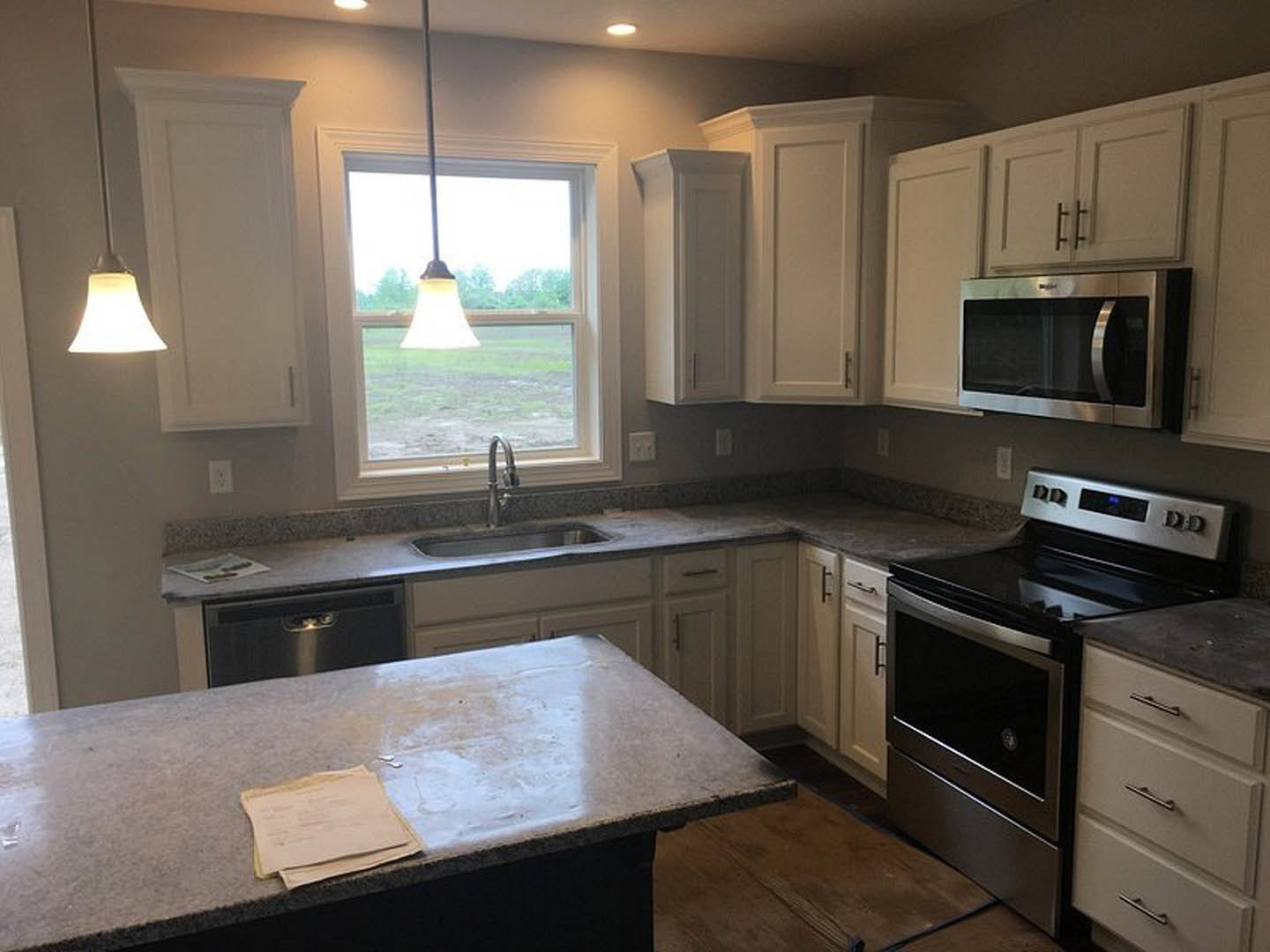 White kitchen cabinets with stone countertop, stainless steel stove and microwave, drawers, stack of papers on counter, sunlight streaming through window