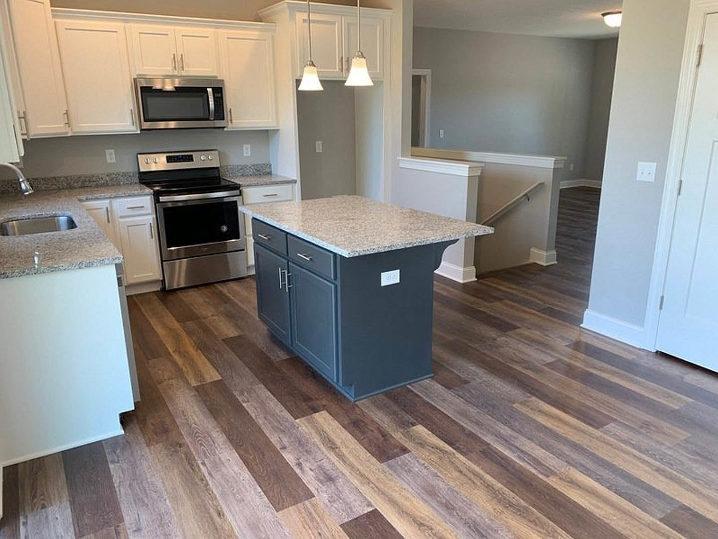 Marble kitchen island with waterfall edge, stainless steel appliances, white cabinetry, pendant lights, hardwood flooring